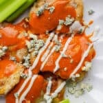 A plate filled with buffalo chicken thighs with blue cheese, ranch and celery.
