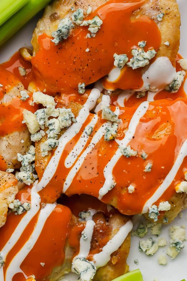 A plate filled with buffalo chicken thighs with blue cheese, ranch and celery.