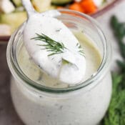 A jar of homemade pickle ranch dressing with a spoon lifting some out with a piece of dill on top.