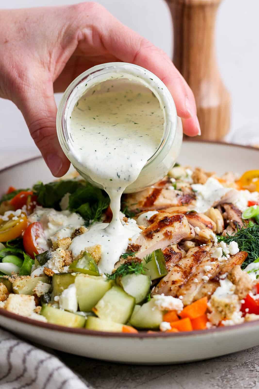 A hand pouring a jar of dill pickle ranch dressing onto dill pickle chicken salad.