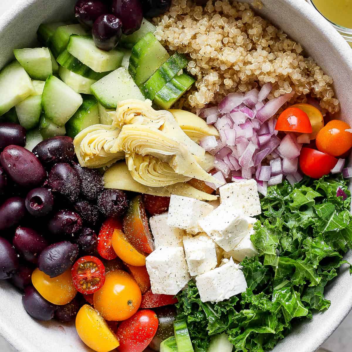Bowl of greek quinoa salad in a bowl with ingredients separated out.