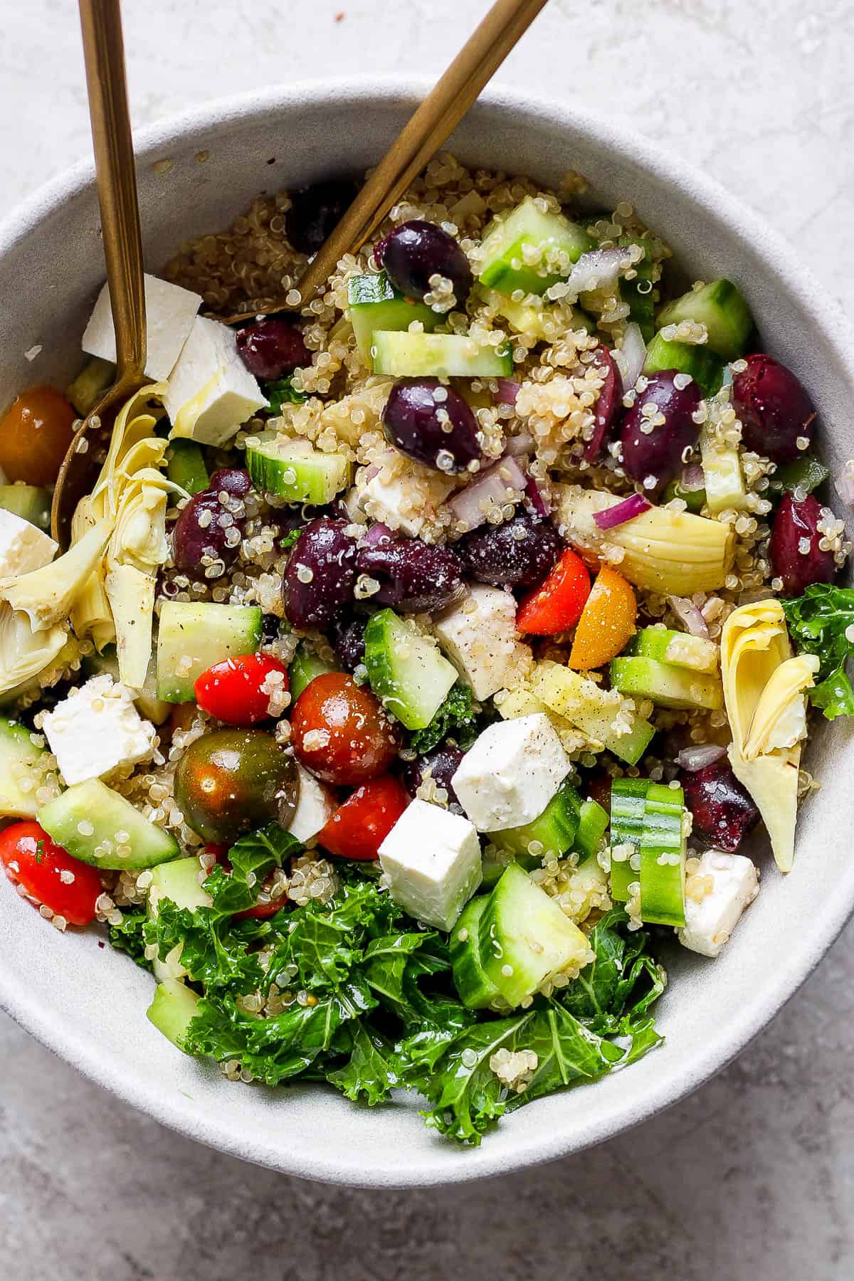 Greek quinoa salad in a bowl with golden spoons.