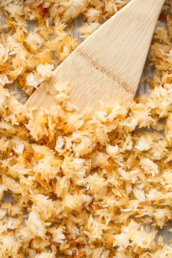 Crispy rice on a baking sheet with a wooden spatula sticking out.