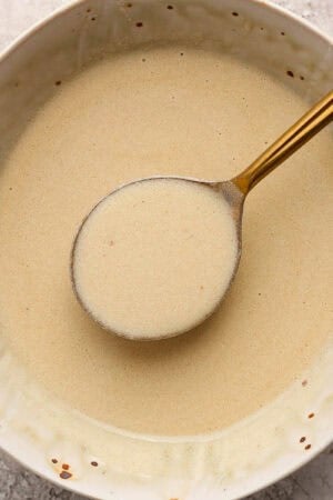A bowl of lemon beurre blanc sauce with a spoon lifting some out.