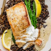 A plate of wild rice, asparagus, lemon wedges, lemon beurre blanc and pan seared halibut.