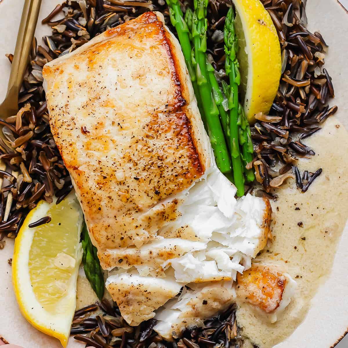 A plate of wild rice, asparagus, lemon wedges, lemon beurre blanc and pan seared halibut.