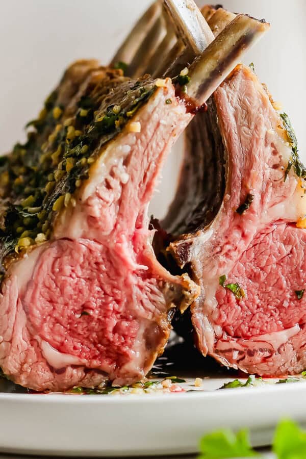 Two racks of lamb on a plate leaning on each other with herbed oil on top.