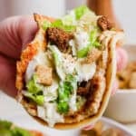 Someone holding a chicken caesar smash burger taco with crushed croutons on top.