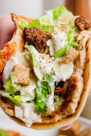Someone holding a chicken caesar smash burger taco with crushed croutons on top.