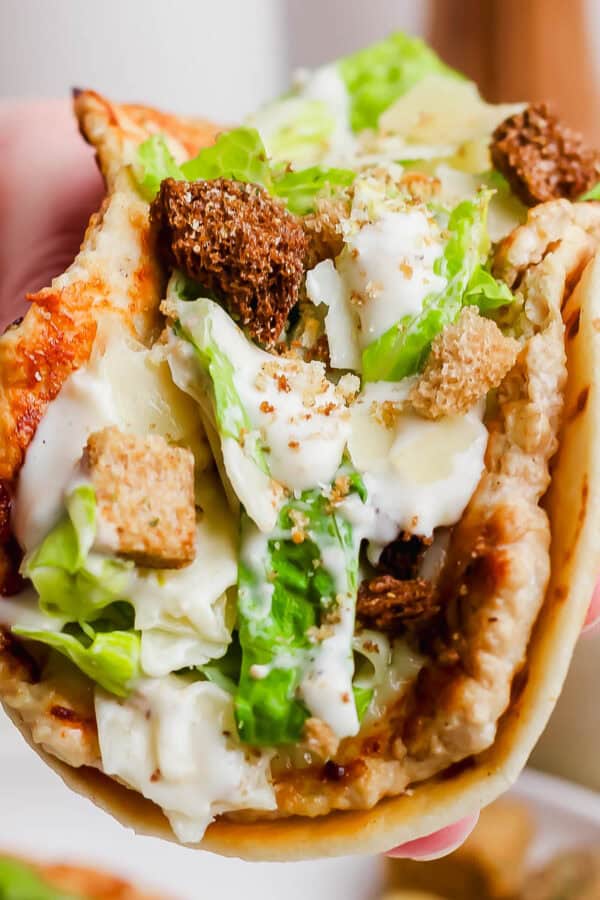 Someone holding a chicken caesar smash burger taco with crushed croutons on top.