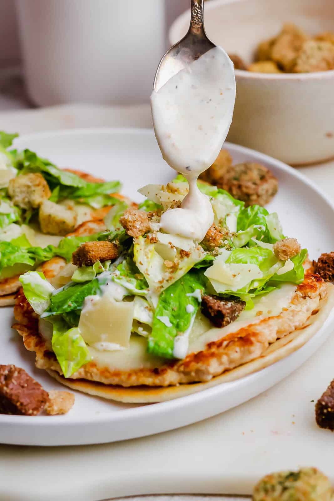 A spoon drizzling caesar dressing over a chicken smash burger taco.