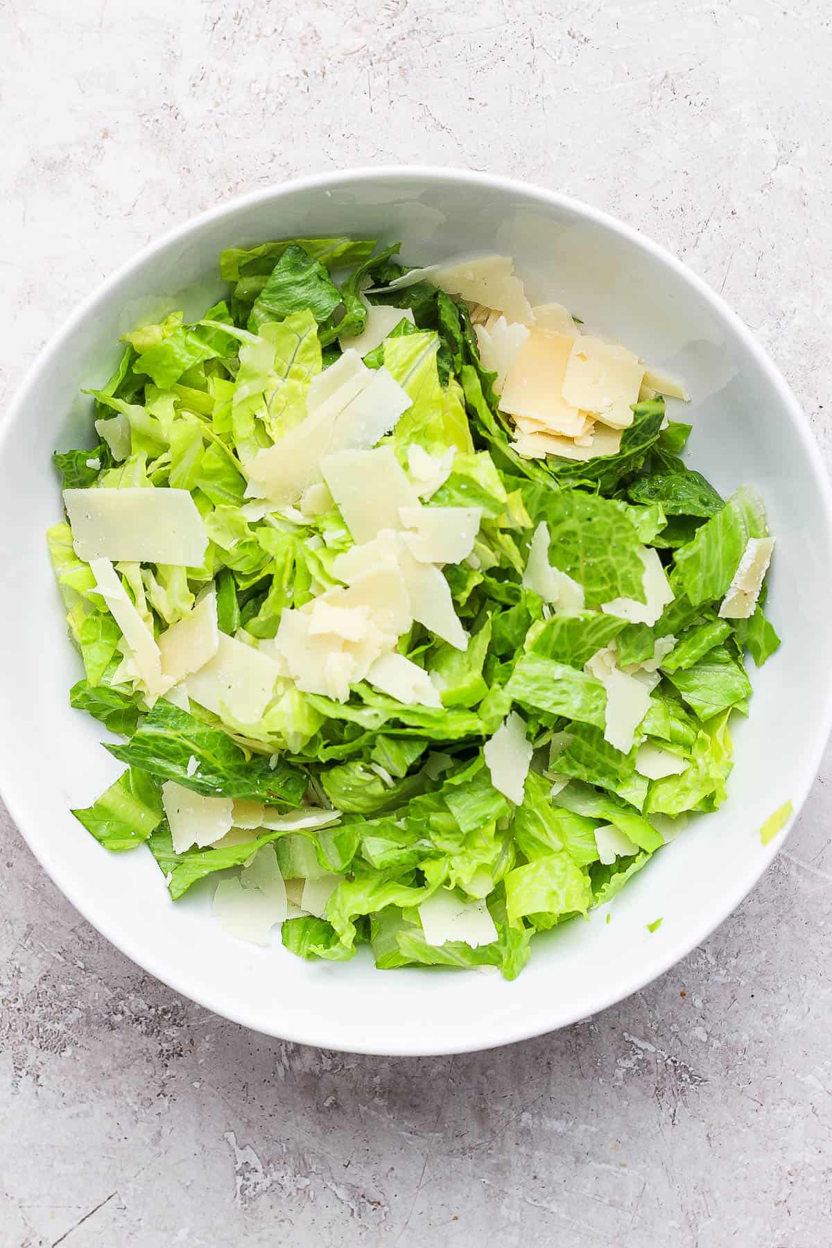 A bowl of chipped romaine topped with shaved parmesan cheese.