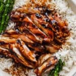A close up of a plate of rice with grilled asparagus and grilled bourbon chicken on top.
