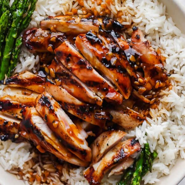 A close up of a plate of rice with grilled asparagus and grilled bourbon chicken on top.