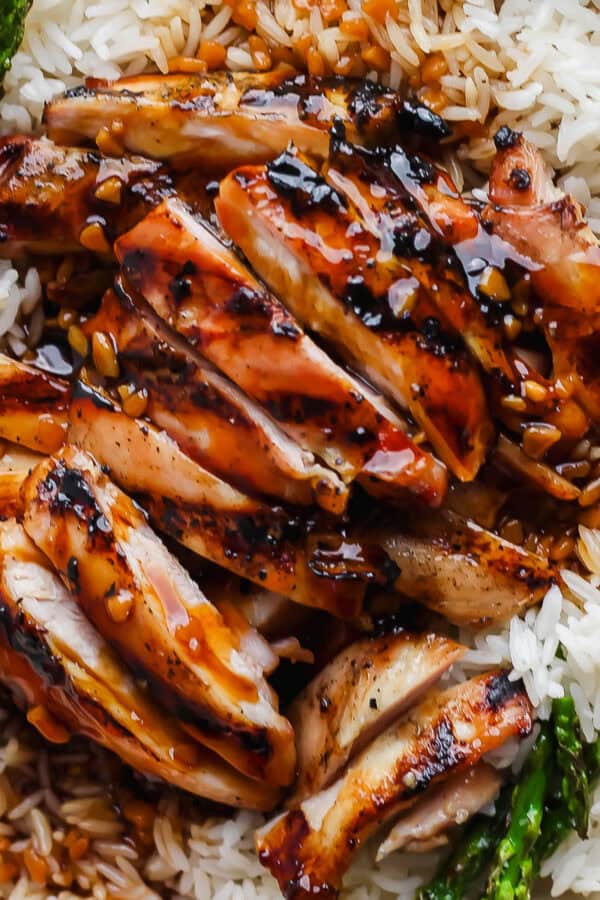 A close up of a plate of rice with grilled asparagus and grilled bourbon chicken on top.