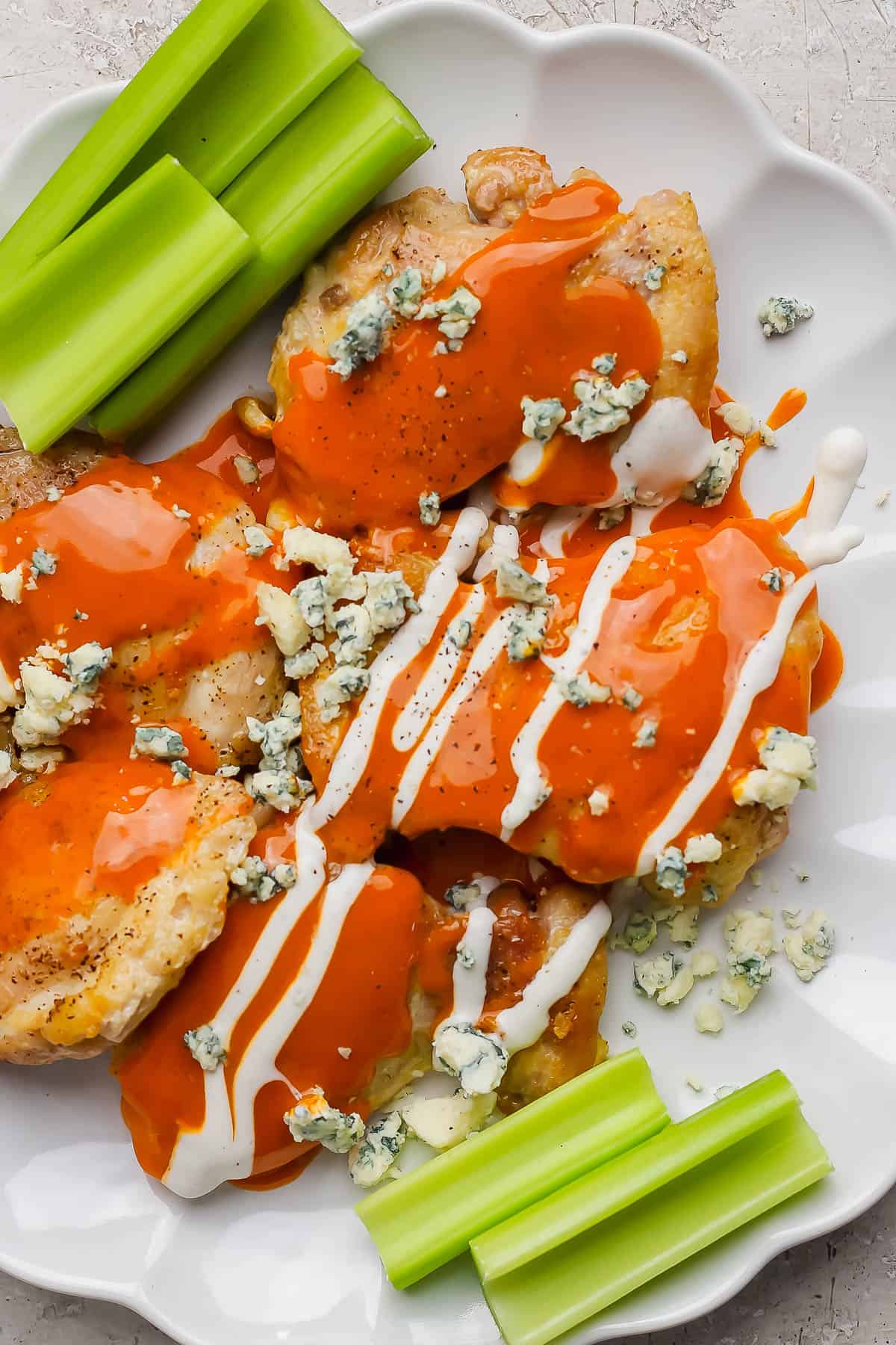 Chicken thighs on a plate topped with buffalo sauce, ranch dressing, and blue cheese.