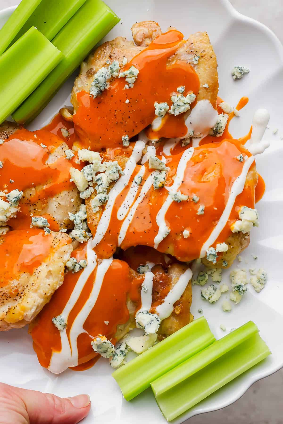 Buffalo chicken thighs on a plate topped with buffalo sauce and blue cheese garnished with celery.