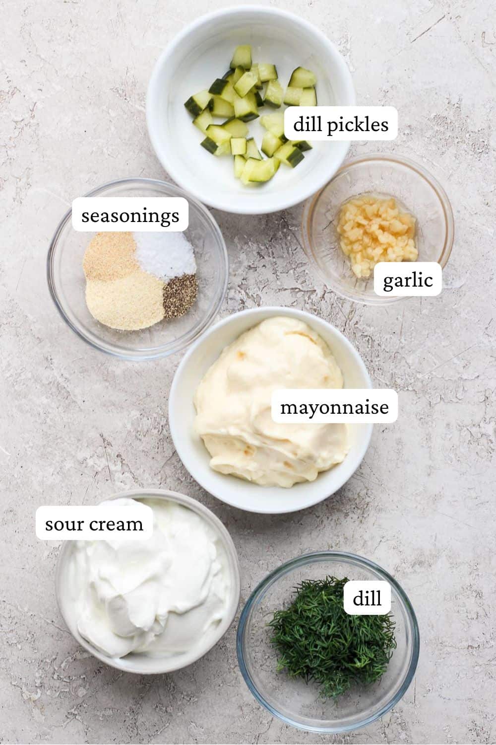 Dill pickle ranch dressing ingredients in individual bowls including chopped dill pickles, garlic, seasonings, mayonnaise, sour cream, and fresh dill.