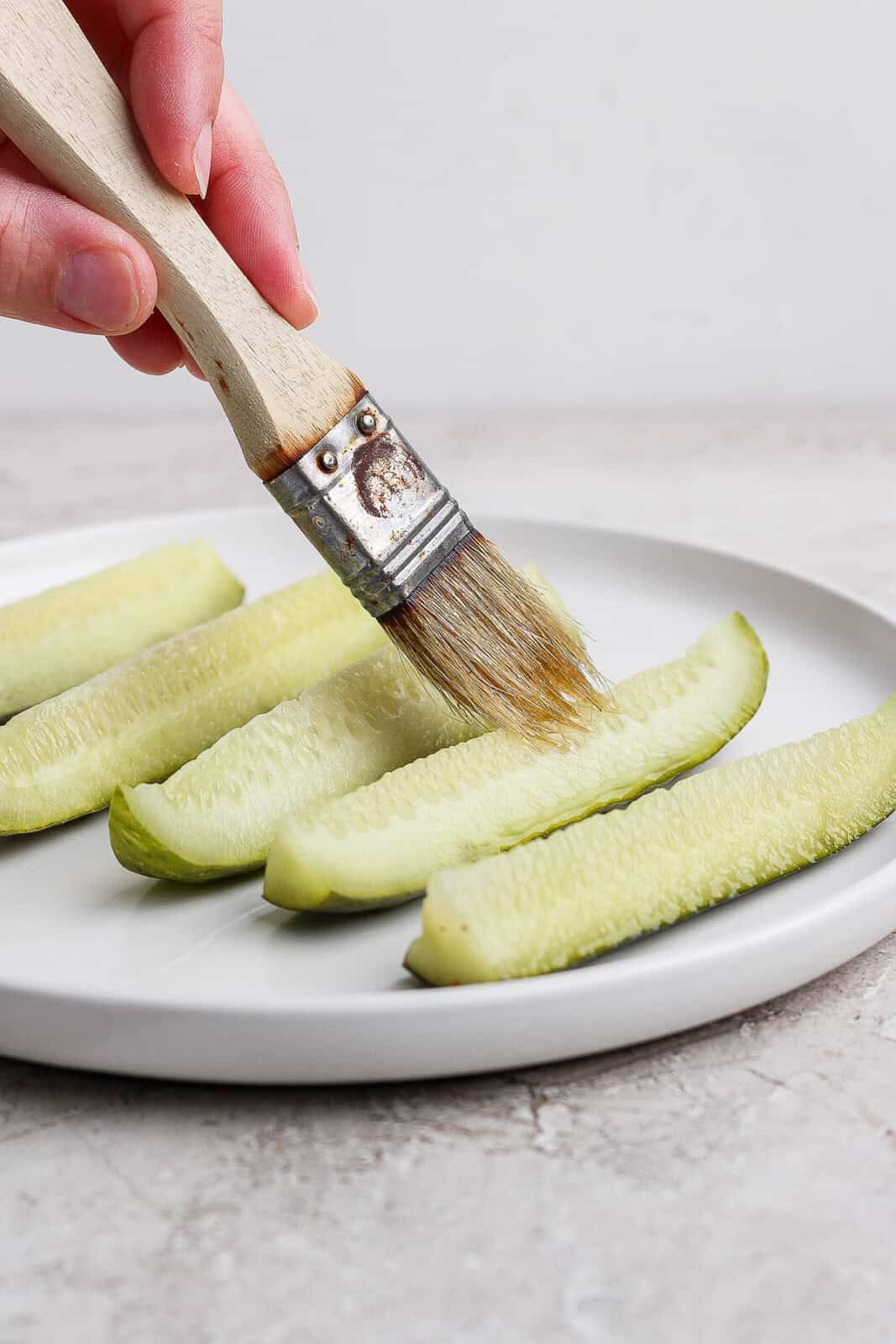 Pickle spears on a plate being brushed with oil