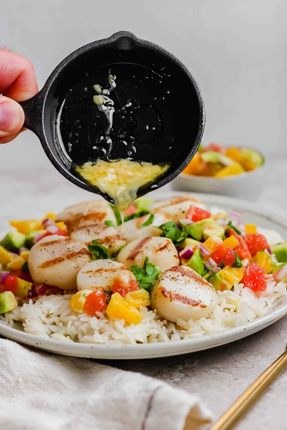 Scallops on a plate with rice, citrus salsa, and melted butter being poured on top.