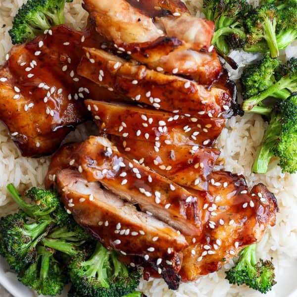 A plate of rice topped with grilled broccoli and grilled teriyaki chicken with sesame seeds on top.