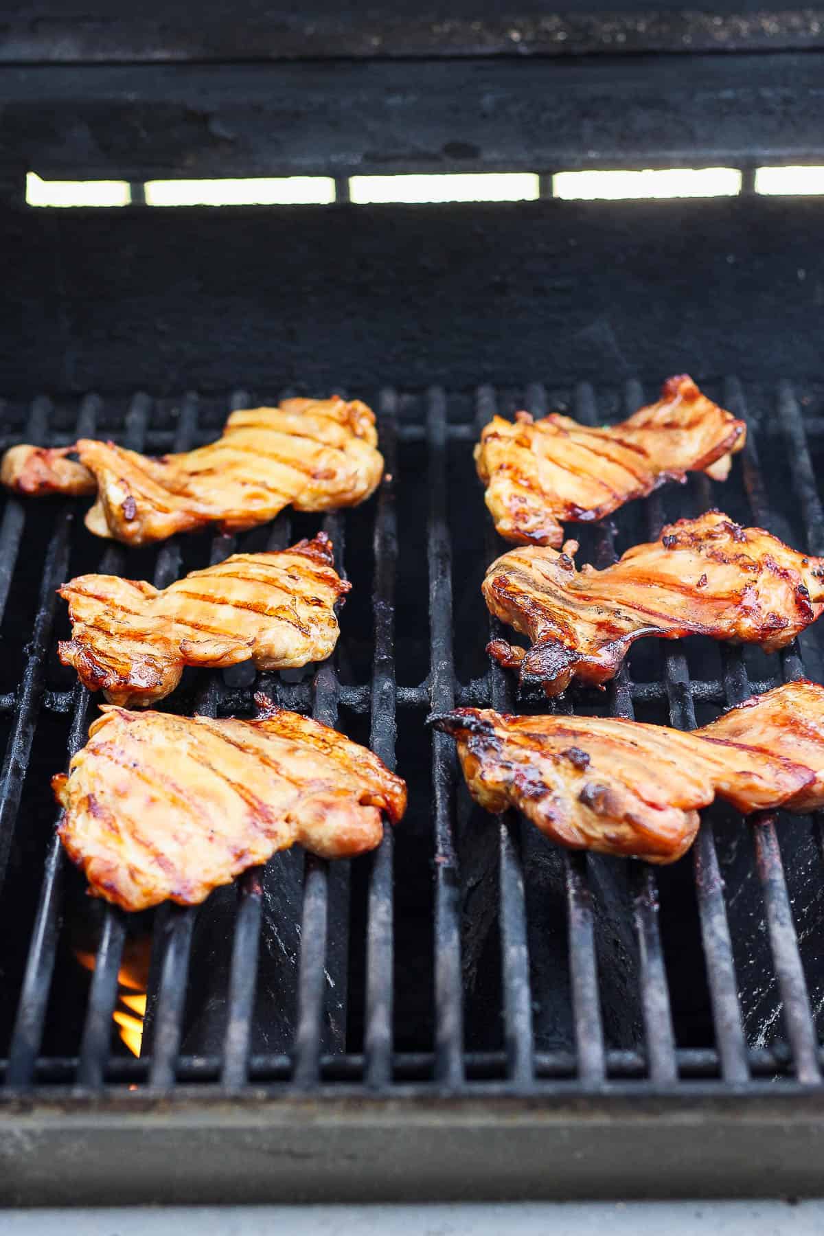 Chicken thighs cooking on a gas grill.