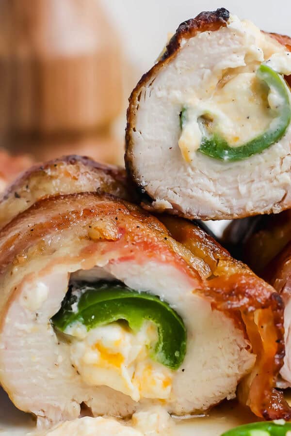 Top pieces of grilled jalapeno popper chicken cut in half on a plate with cheese oozing out.