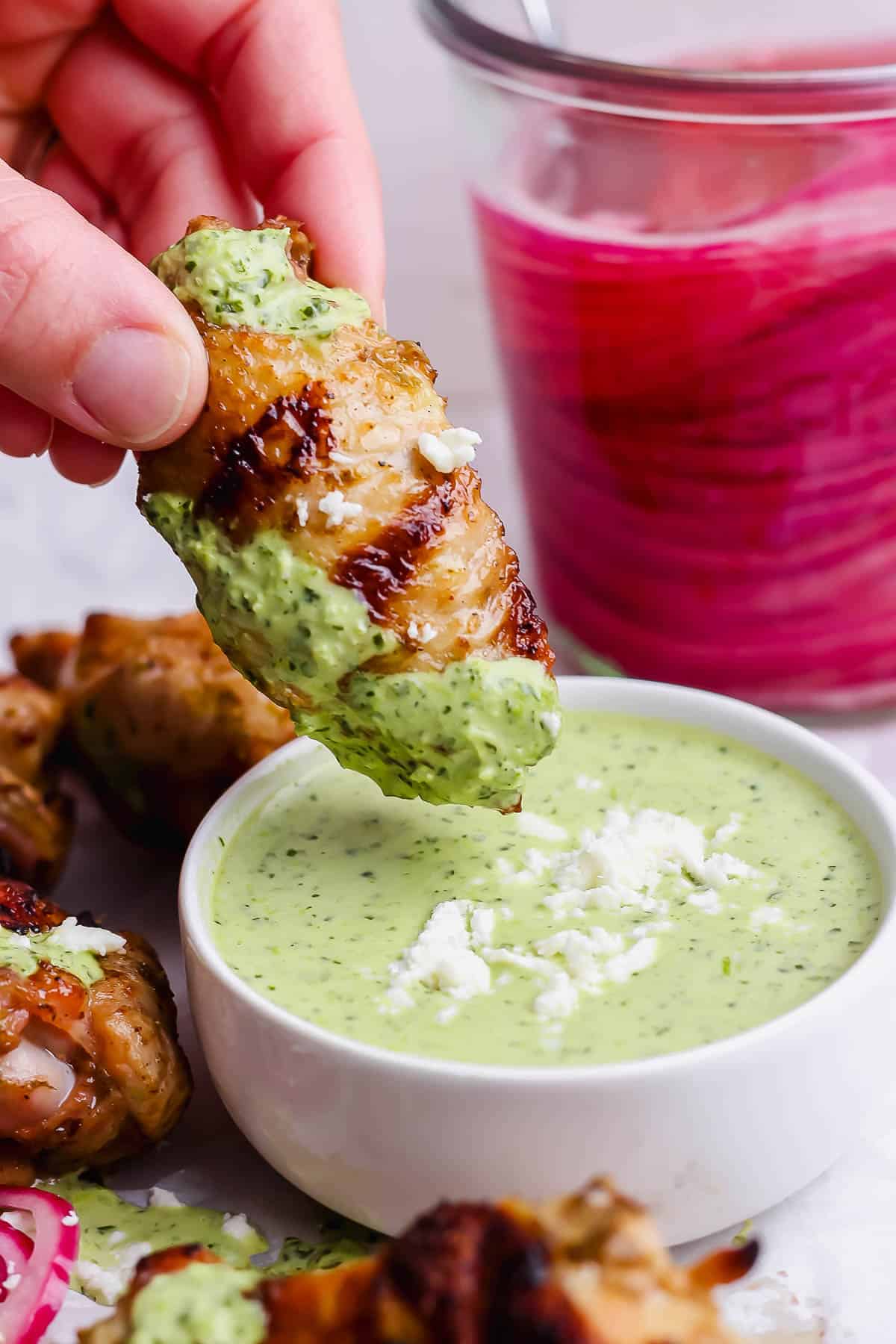 A hand dipping a wing into green sauce.