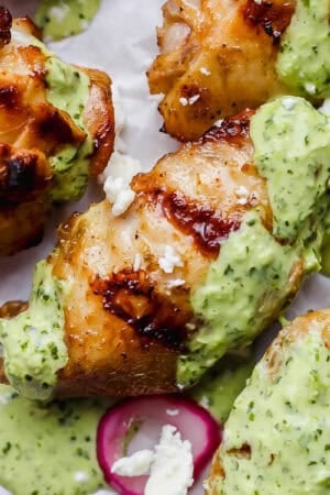 Grilled peruvian chicken wings on a piece of parchment paper with green sauce, feta and pickled onions.