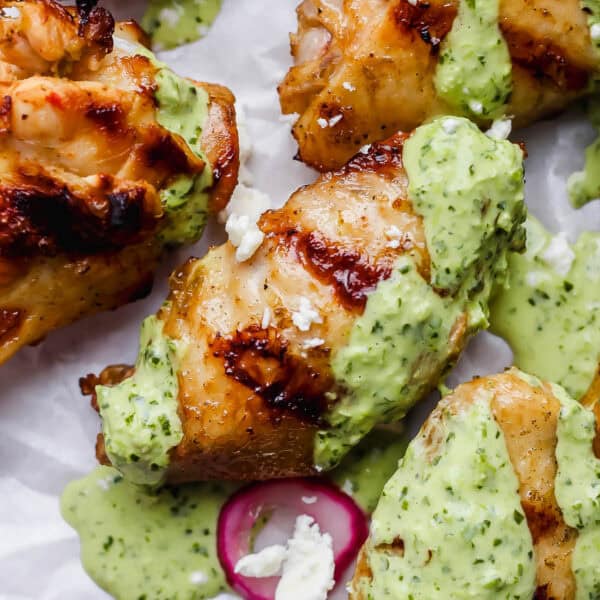 Grilled peruvian chicken wings on a piece of parchment paper with green sauce, feta and pickled onions.