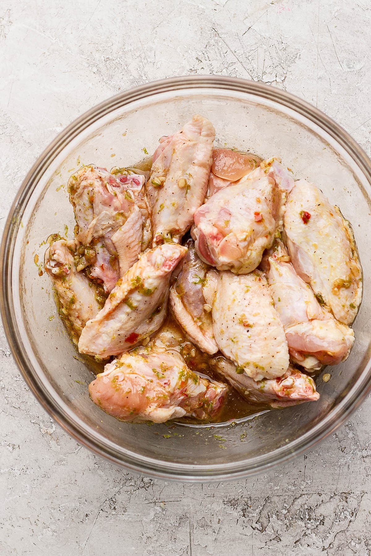 Chicken wings in a glass bowl with marinade ingredients over the top.