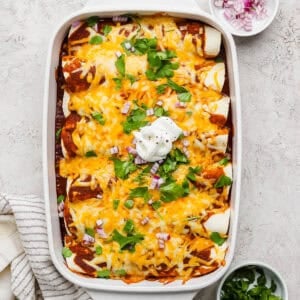 A top shot of casserole dish filled with pulled pork enchiladas topped with cilantro, red onion and sour cream.