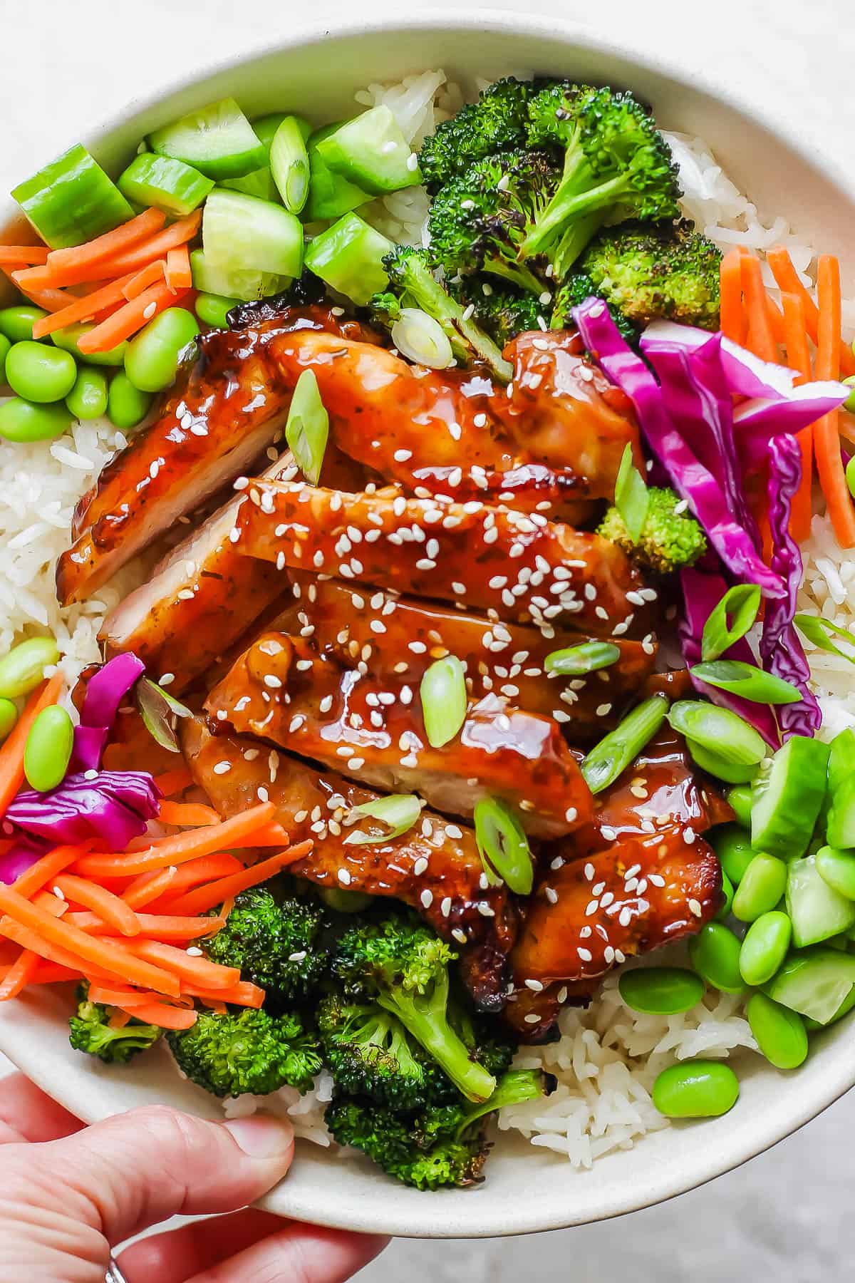 Teriyaki Chicken Bowls - simple and delicious weeknight dinner (or meal prep!) that your whole family will love! (Whole30, Paleo, GF + DF) #teriyakichickenbowls #teriyakichickenbowl #whole30dinner #instantpotmeals #paleodinner #healthychickendinner A hand holding a teriyaki chicken bowl.