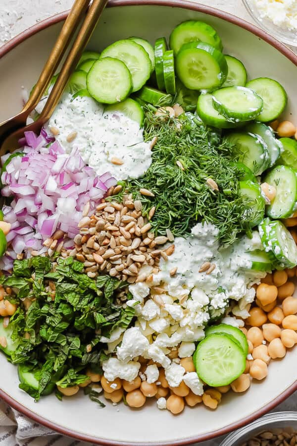 A bowl of Cucumber Chickpea Salad with sunflower seeds, feta and herbs with a spoon sticking out.
