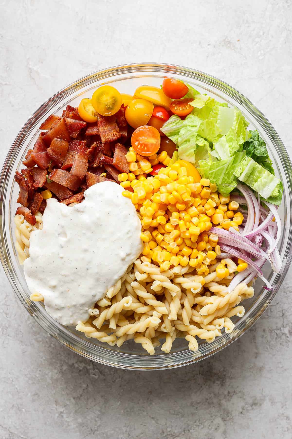 A large glass bowl of all the pasta salad ingredients before mixing.