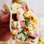 Someone holding a grilled steak taco with cilantro lime rice, grilled corn, steak and chipotle lime sauce.