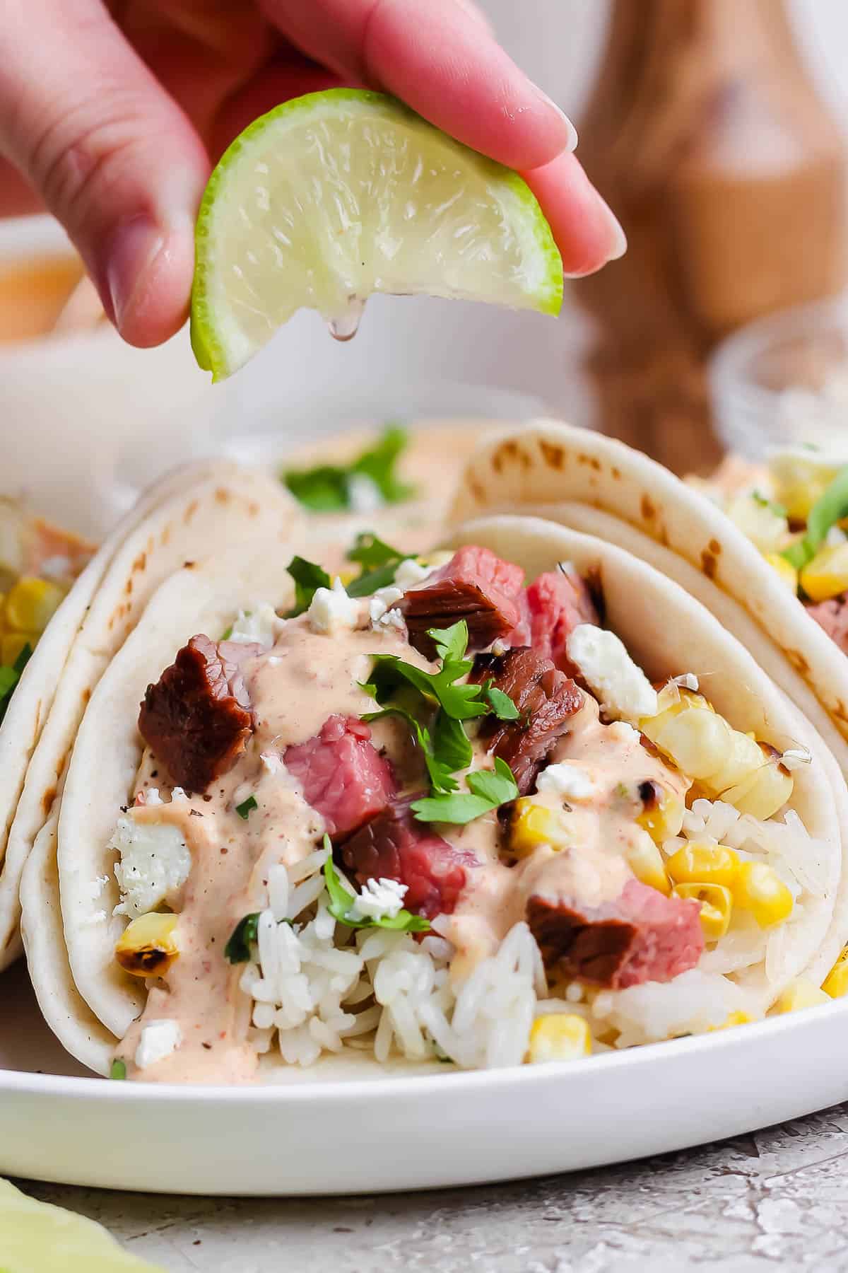 A hand squeezing a lime wedge over a grilled steak taco.
