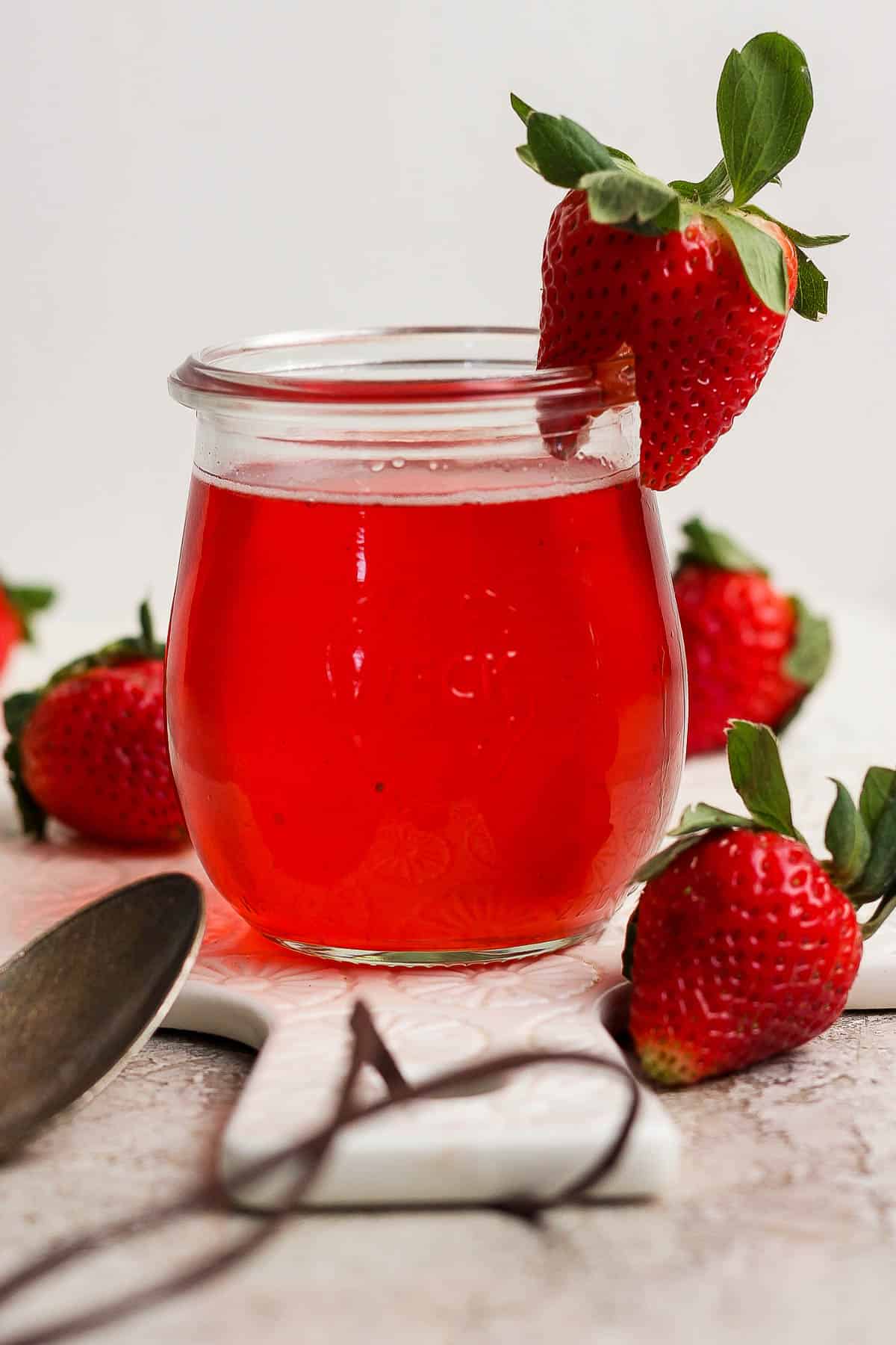 Strawberry simple syrup in a small jar surrounded by fresh strawberries.