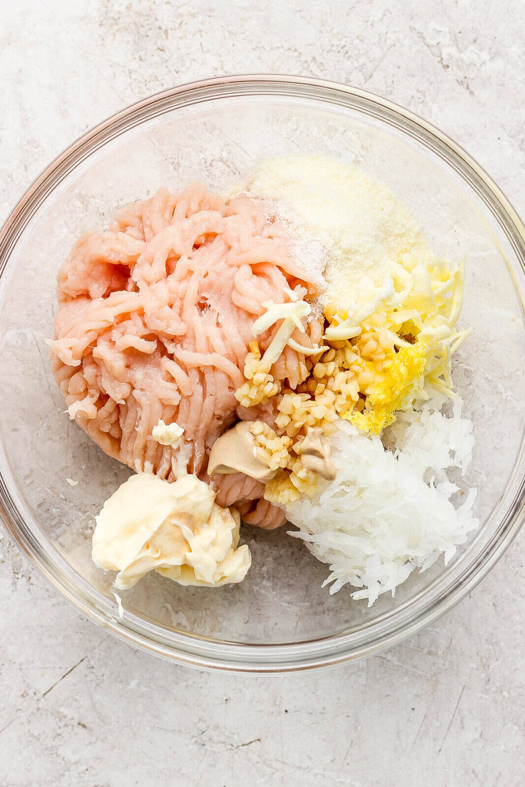 Ground chicken, mayo, garlic, onion, lemon, and parmesan in a bowl unmixed.