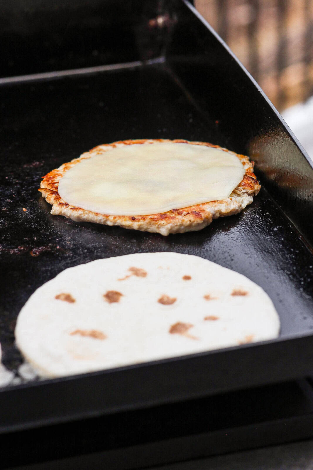 The chicken patty on top of a tortilla topped with a slice of cheese.