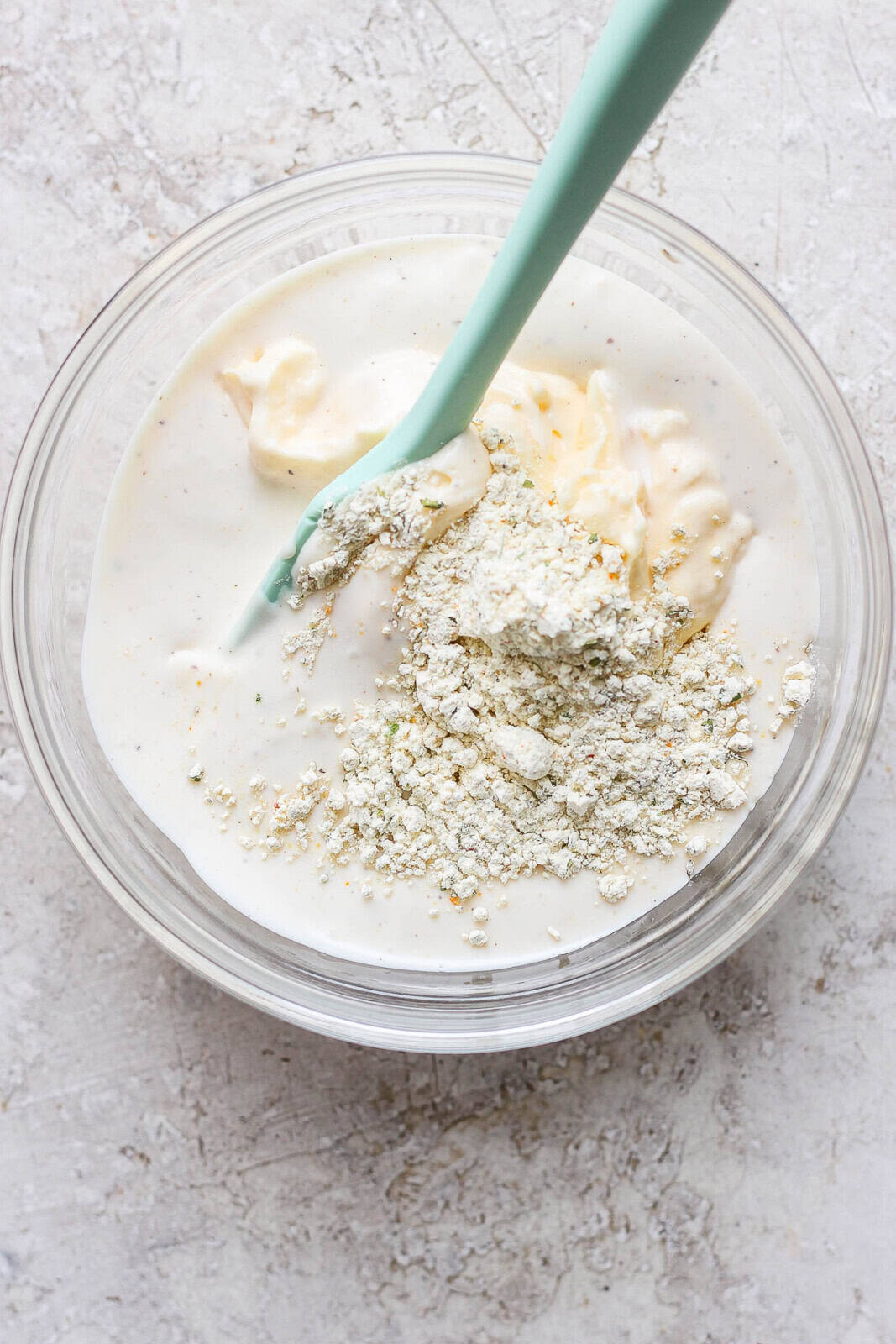 Ranch seasoning, mayo, and ranch dressing in a bowl with a spatula.