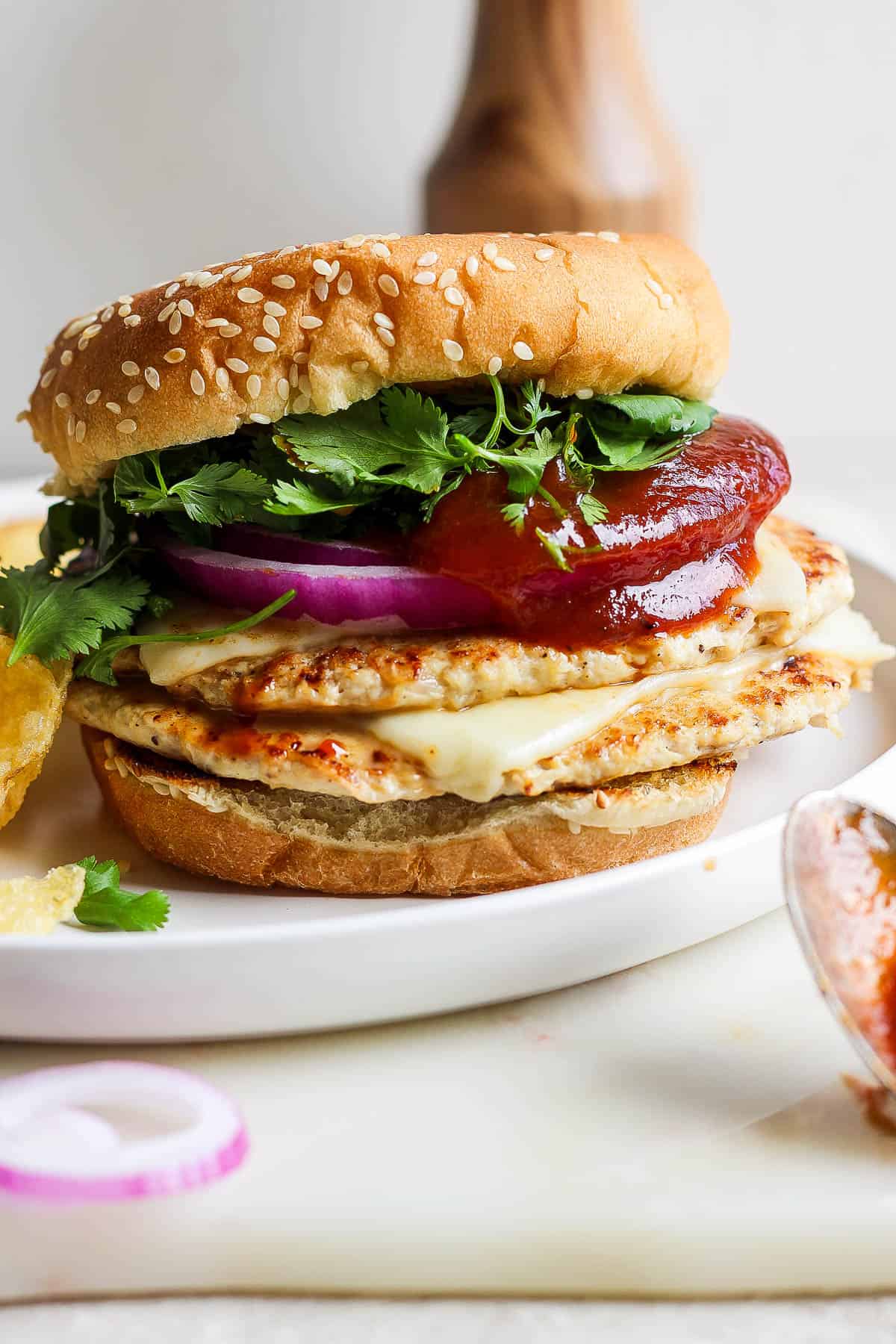 A fully assembled BBQ chicken smash burger on a white plate.