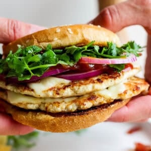 Someone holding a bbq chicken smash burger taco with red onion, bbq sauce and cilantro.