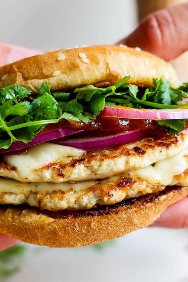 Someone holding a bbq chicken smash burger taco with red onion, bbq sauce and cilantro.