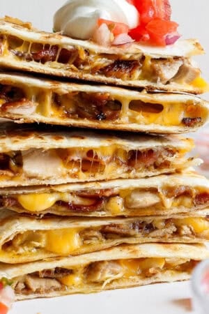 A stack of chicken bacon ranch quesadillas with pico de gallo and sour cream.
