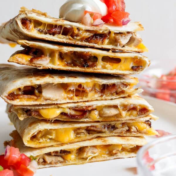A stack of chicken bacon ranch quesadillas with pico de gallo and sour cream.