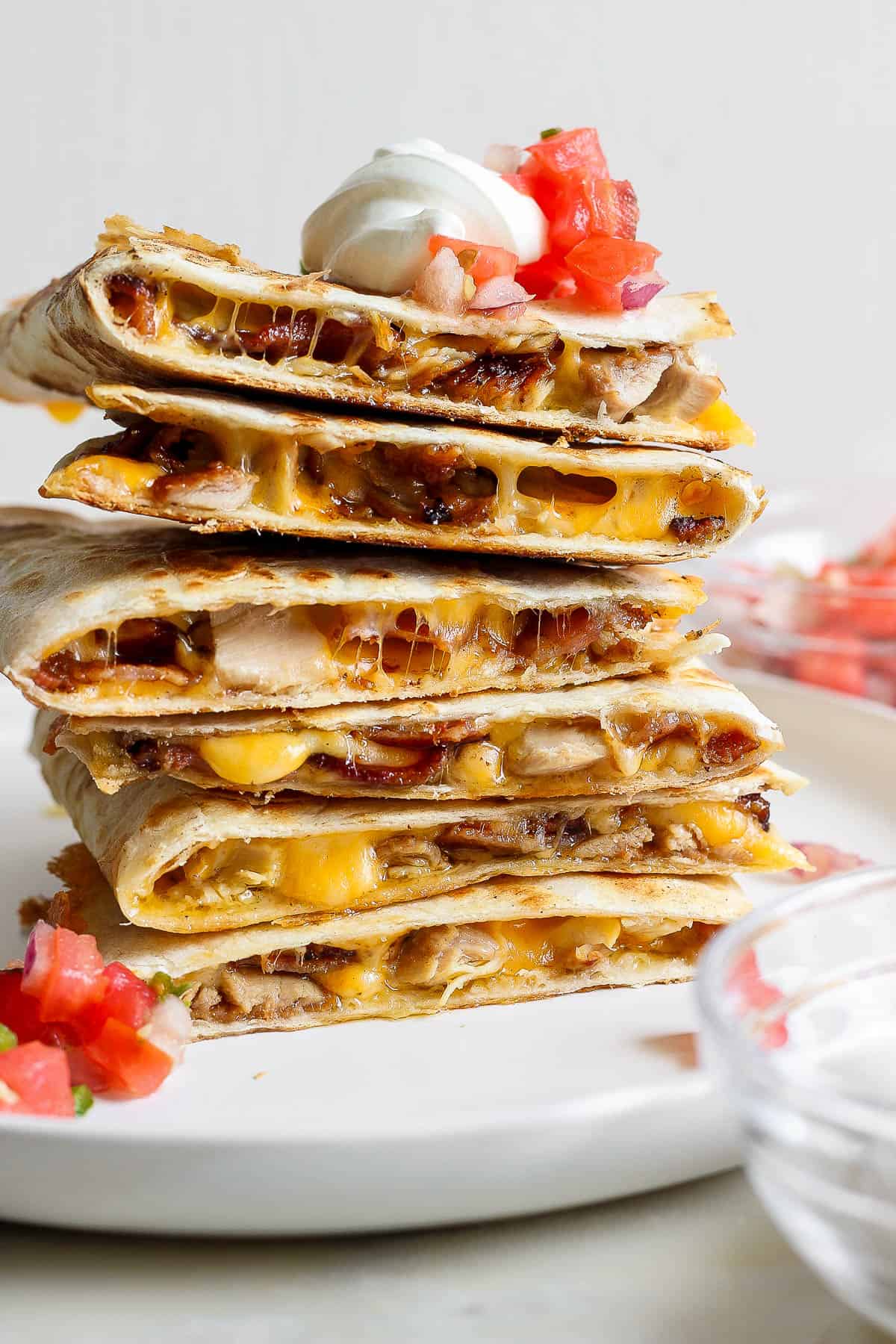 A stack of chicken, bacon ranch quesadillas topped with pico and sour cream.