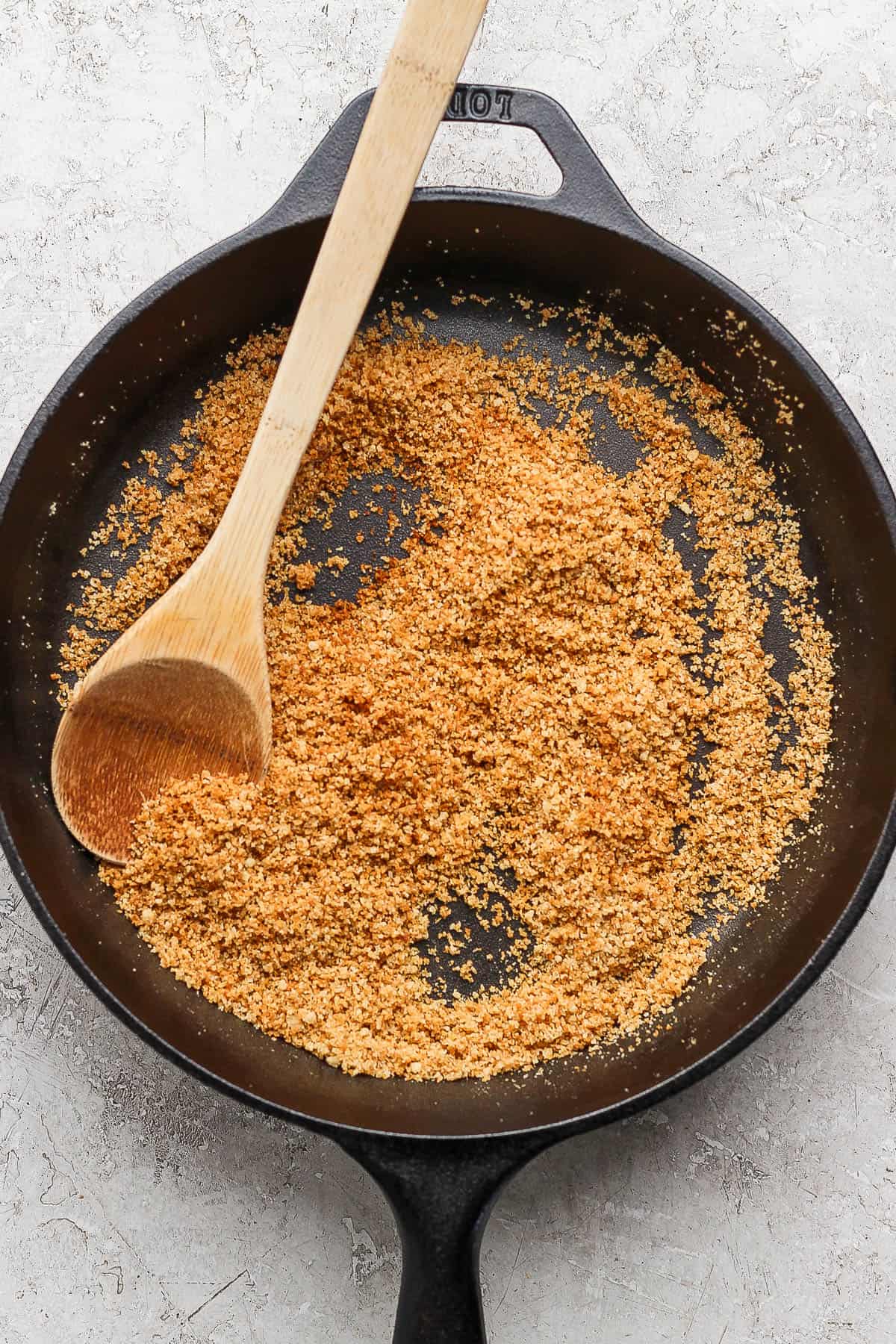 Browned breadcrumbs in a cast iron skillet with a wooden spoon.