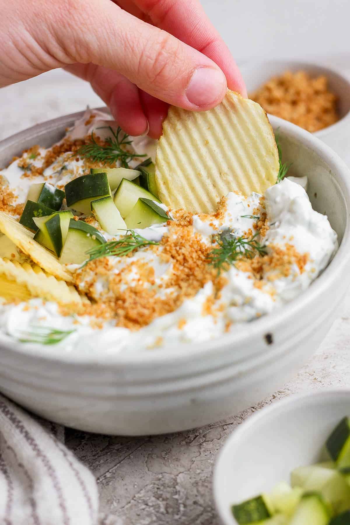A hand scooping the dip with a potato chip.
