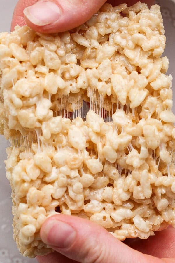 Someone holding an extra gooey rice krispie treat and pulling it apart.